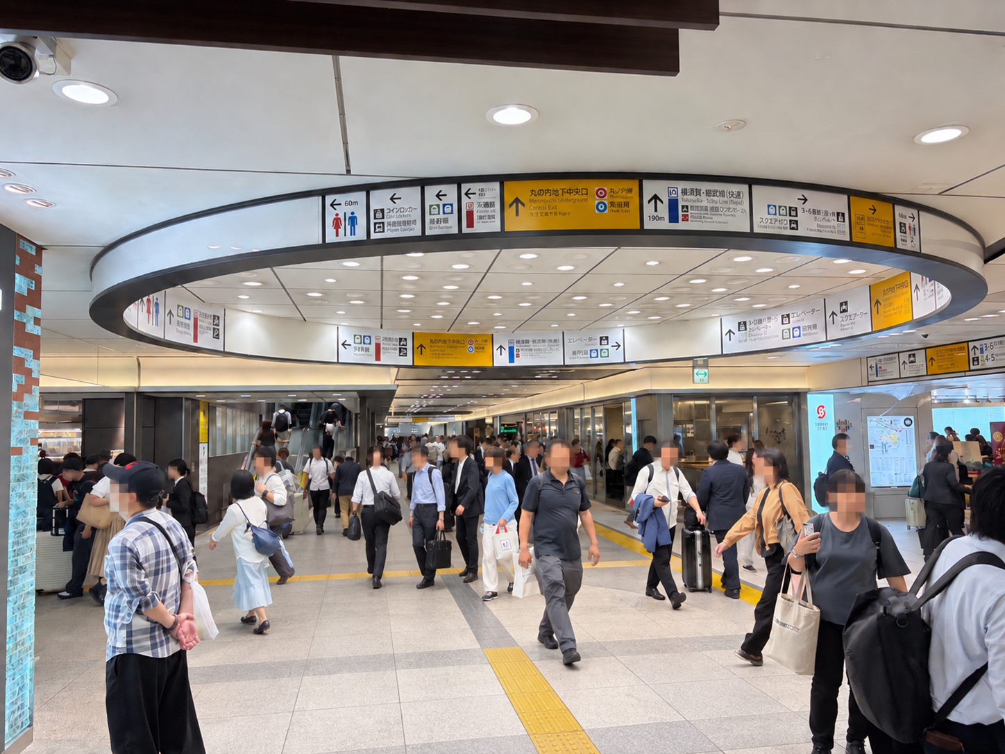 案内表示が並ぶ大規模な駅のコンコース。黄色い点字ブロックに沿って、多くの利用者が行き交っている。