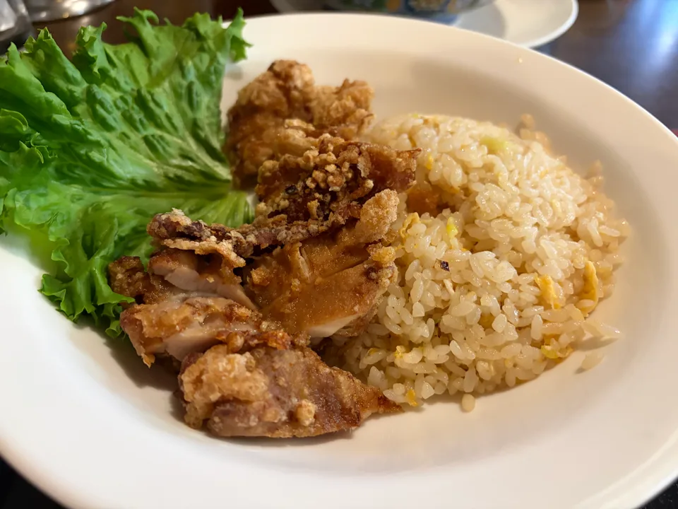 白い皿に、揚げた鶏肉と葉野菜、卵入りの炒めご飯が盛り付けられている。