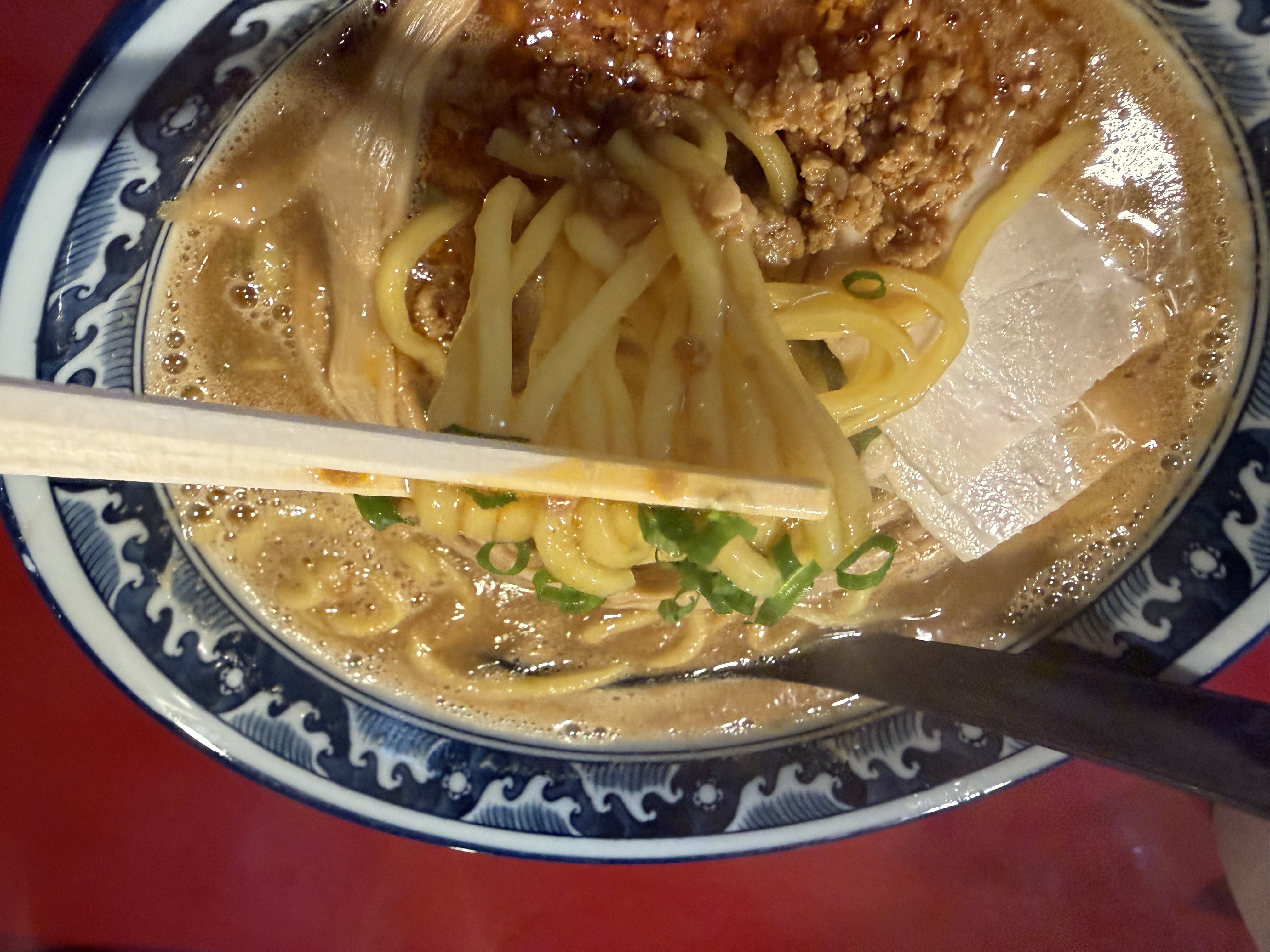 青ねぎとひき肉、薄切りの具材がのったスープ麺を、箸で持ち上げている様子。